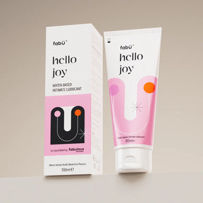 Packaging of "Hello Joy" water-based intimate lubricant is shown. A 100ml pink and white box and tube are displayed against a neutral background.