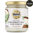 A jar of Biona Organic Raw Virgin Coconut Oil with a gold lid and tropical design, featuring palm leaves and coconut imagery. It has a "Great Taste 2024" award badge.
