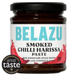 A jar of Belazu Smoked Chilli Harissa Paste on a white background, featuring a black lid, dark brown glass, and a white label with turquoise and red text and chili graphics. A circular 'great taste 2025' badge is overlaid in the bottom-left corner.