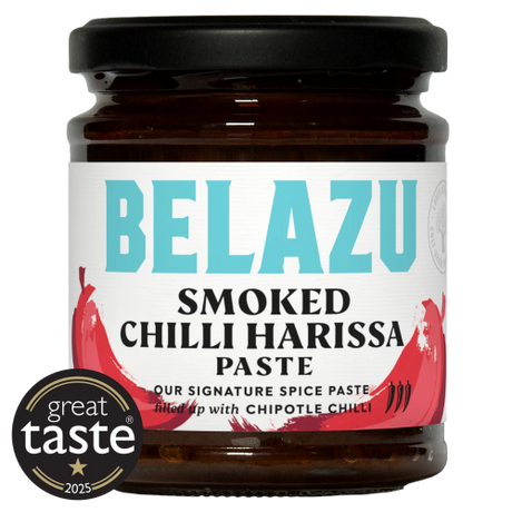 A jar of Belazu Smoked Chilli Harissa Paste on a white background, featuring a black lid, dark brown glass, and a white label with turquoise and red text and chili graphics. A circular 'great taste 2025' badge is overlaid in the bottom-left corner.