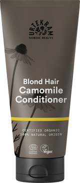 A dark grey squeeze tube of Urtekram Camomile Conditioner for blond hair with a black cap. The label features camomile flower illustrations, a thin yellow horizontal stripe, and specifies it is certified organic and 100% natural origin, with Vegan and Ecocert COSMOS Organic certifications.