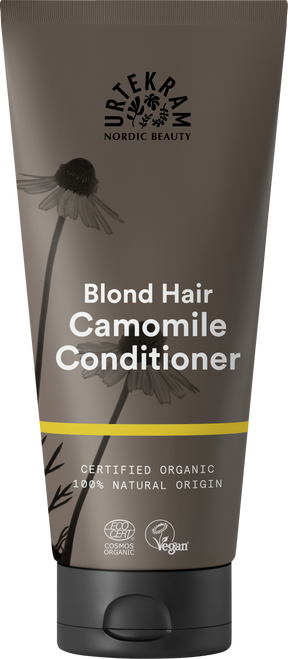A dark grey squeeze tube of Urtekram Camomile Conditioner for blond hair with a black cap. The label features camomile flower illustrations, a thin yellow horizontal stripe, and specifies it is certified organic and 100% natural origin, with Vegan and Ecocert COSMOS Organic certifications.