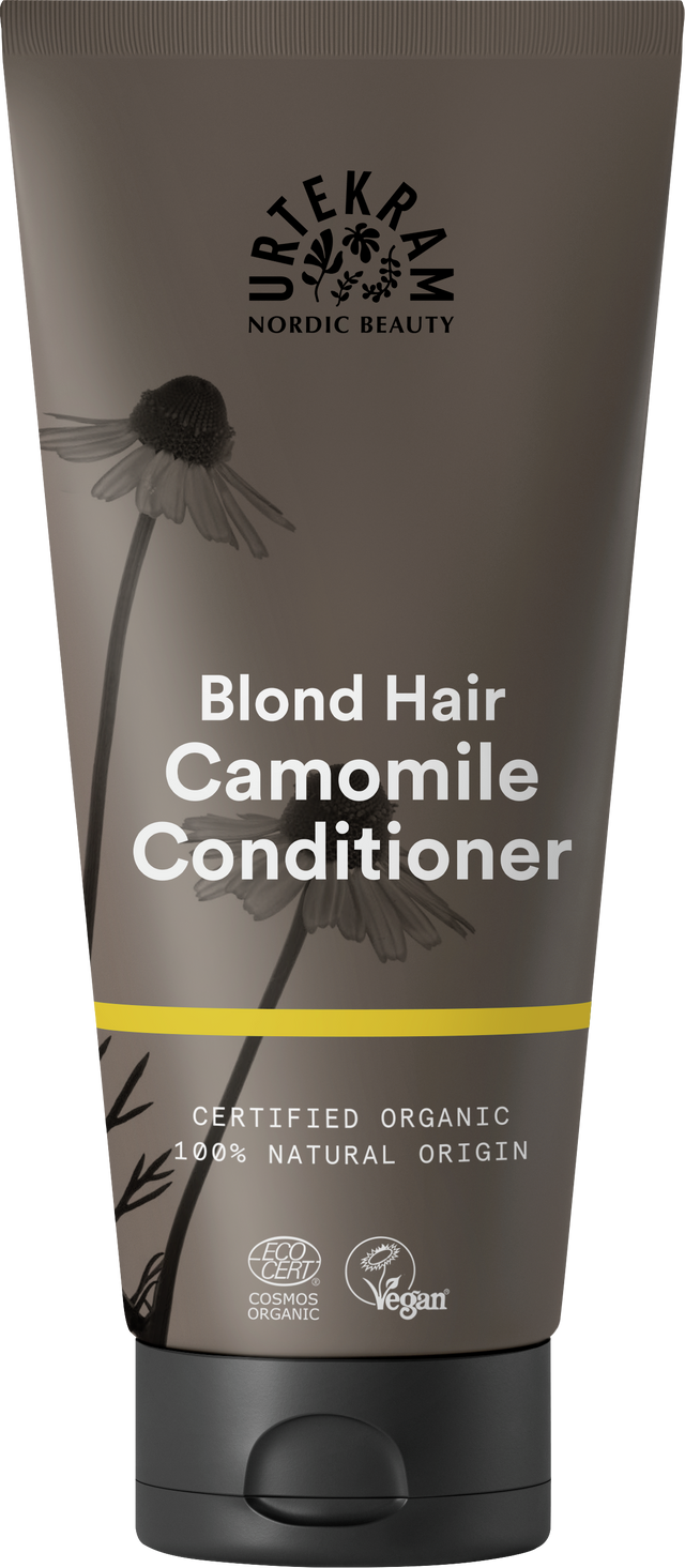 A dark grey squeeze tube of Urtekram Camomile Conditioner for blond hair with a black cap. The label features camomile flower illustrations, a thin yellow horizontal stripe, and specifies it is certified organic and 100% natural origin, with Vegan and Ecocert COSMOS Organic certifications.