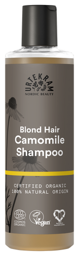 A tall bottle of Urtekram Camomile Shampoo for blond hair with a grey and brown label featuring camomile flower illustrations and a thin yellow horizontal stripe. The label indicates it is certified organic, 100% natural origin, and carries Vegan and Ecocert COSMOS Organic certifications.