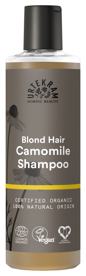 A tall bottle of Urtekram Camomile Shampoo for blond hair with a grey and brown label featuring camomile flower illustrations and a thin yellow horizontal stripe. The label indicates it is certified organic, 100% natural origin, and carries Vegan and Ecocert COSMOS Organic certifications.