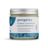 A jar of Georganics mineral toothpaste in English Peppermint flavor, featuring a silver lid and a blue leaf-patterned label, emphasizes natural ingredients.