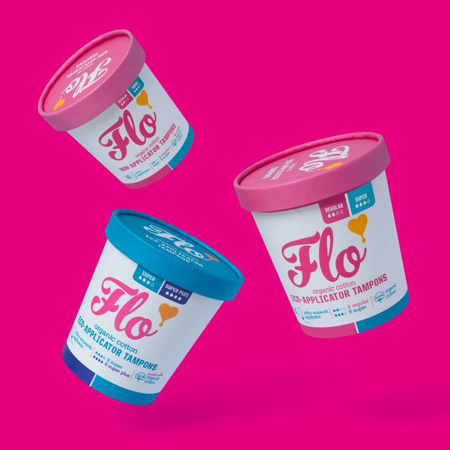 Floating on a vibrant pink background, three cylindrical Flo tampon containers with pink and blue lids. Energetic, modern design elements.