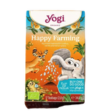A box of Yogi Organic Happy Farming tea sits on a wicker tray beside a cup of tea. A plate with vanilla pods and a flower is nearby. The scene feels cozy and inviting.