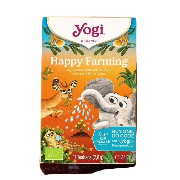 A box of Yogi Organic Happy Farming tea sits on a wicker tray beside a cup of tea. A plate with vanilla pods and a flower is nearby. The scene feels cozy and inviting.