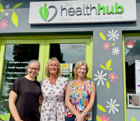 Three women standing in front of a building with 'The Health Hub' sign.