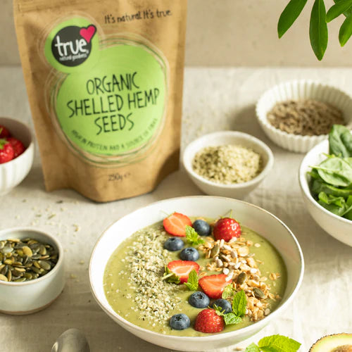 Green smoothie bowl topped with berries and hemp seeds, next to a bag of True Organic Shelled Hemp Seeds.