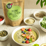 Green smoothie bowl topped with berries and hemp seeds, next to a bag of True Organic Shelled Hemp Seeds.