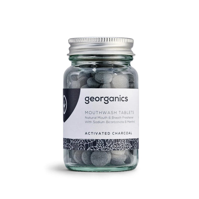 A jar of Georganics activated charcoal mouthwash tablets with a silver lid. The label is white with botanical designs and black text.