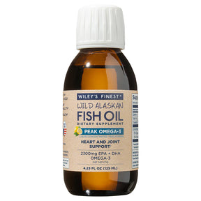 An amber glass bottle of Wiley's Finest Wild Alaskan Fish Oil with a white cap. The label features a lemon illustration and specifies it is "Peak Omega-3" liquid concentrated triglyceride for heart and joint support, providing 2300mg EPA + DHA per serving.