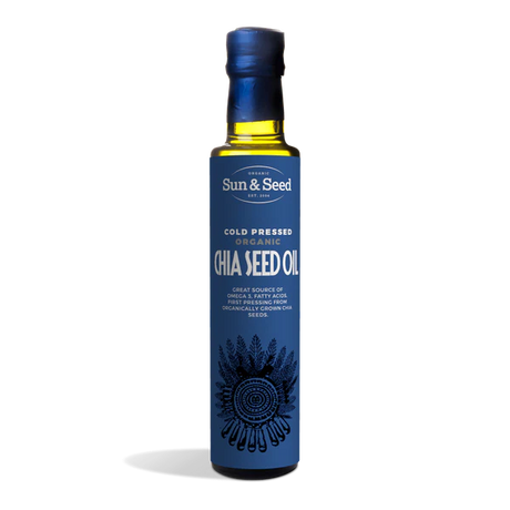 Tall dark glass bottle of Sun & Seed Cold Pressed Organic Chia Seed Oil featuring a deep blue label with an intricate feathered circular graphic at the bottom.