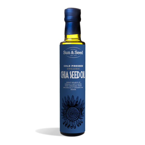 Tall dark glass bottle of Sun & Seed Cold Pressed Organic Chia Seed Oil featuring a deep blue label with an intricate feathered circular graphic at the bottom.