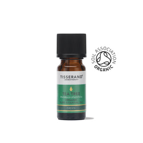 A small amber glass bottle of Tisserand Tea Tree organic pure essential oil with a green and white label and a black cap.