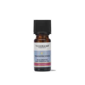 A small amber glass bottle of Tisserand Frankincense wild crafted pure essential oil with a light blue and white label and a black cap.