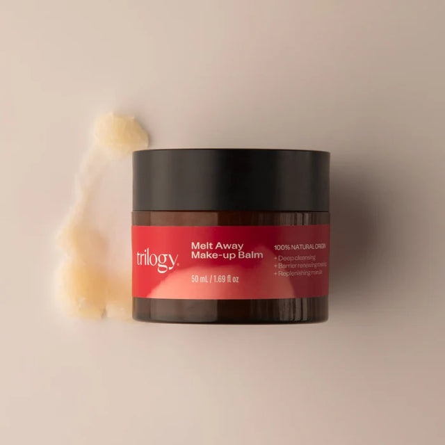 A dark amber jar of Trilogy Melt Away Make-up Balm with a black lid, accompanied by a textured scoop of the pale, buttery balm. 