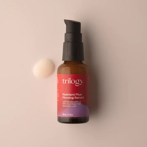 A small amber glass bottle of Trilogy Nutrient Plus Firming Serum with a black pump dispenser, positioned against a soft beige background.