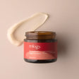 An open amber glass jar of Trilogy Rosapene™ Night Cream, accompanied by a thick, curved smear of the creamy white moisturizer. 