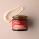 An open amber glass jar of Trilogy Rosapene™ Night Cream, accompanied by a thick, curved smear of the creamy white moisturizer. 