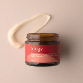 An open amber glass jar of Trilogy Rosapene™ Night Cream, accompanied by a thick, curved smear of the creamy white moisturizer. 