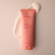 A tube of Trilogy Rosehip Cream Cleanser in a soft coral-pink matte finish, positioned over a thick, creamy white product swatch on a matching pastel background.