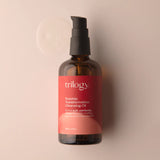 An amber glass bottle of Trilogy Rosehip Transformation Cleansing Oil with a black pump dispenser, set against a soft beige background.