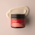 An amber glass jar of Trilogy Vital Moisturising Cream with a black lid, accompanied by a thick, sweeping smear of the creamy white moisturizer behind it.