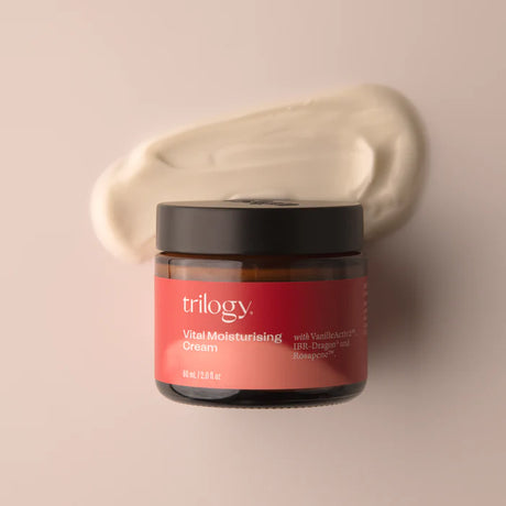 An amber glass jar of Trilogy Vital Moisturising Cream with a black lid, accompanied by a thick, sweeping smear of the creamy white moisturizer behind it.