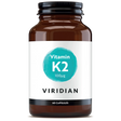 A 60-capsule amber glass jar of Viridian Vitamin K2 100µg food supplement with a white label and a turquoise watercolor-style circle, isolated on a white background.