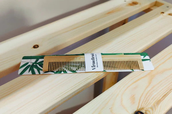 VirtueBrush sustainable bamboo pocket comb on a light wooden slatted surface.