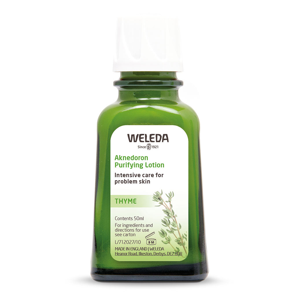 A small, green glass bottle of Weleda Aknedoron Purifying Lotion featuring a white label with a sprig of thyme, marketed as intensive care for problem skin.
