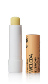 An open tube of Weleda Everon Lip Balm showing the pale yellow balm stick next to its peach-colored cap featuring the brand name and "Lippenpflege" text.