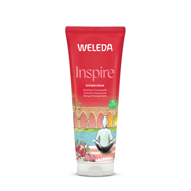 A red 200ml tube of Weleda Inspire Shower Cream featuring "Sensual Pomegranate" text and an illustration of a person meditating by a pool with pomegranate fruit in the foreground.