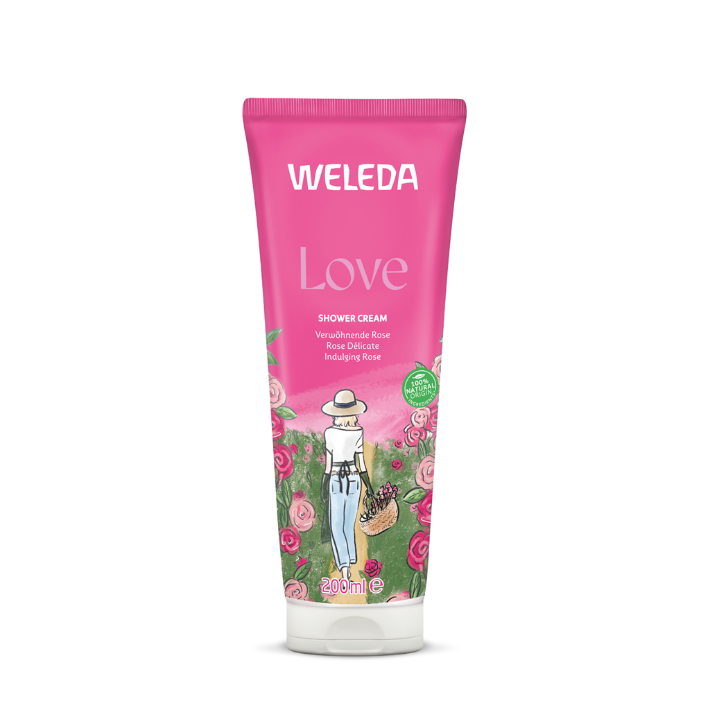 A pink 200ml tube of Weleda Love Shower Cream featuring "Indulging Rose" text and an illustration of a woman in a sun hat carrying a basket of pink roses through a garden.