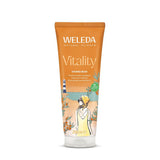 An orange tube of Weleda Vitality Shower Cream featuring a summer-themed illustration of a woman at a beach with a lighthouse and sea buckthorn plants.