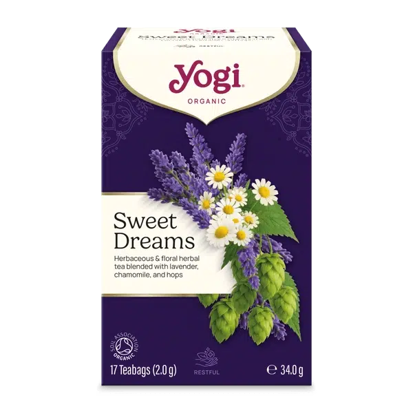 A box of Yogi Organic Sweet Dreams herbal tea blend, featuring a deep purple background with illustrations of lavender, chamomile, and hops alongside white daisies. The Yogi brand logo is clearly visible at the top.