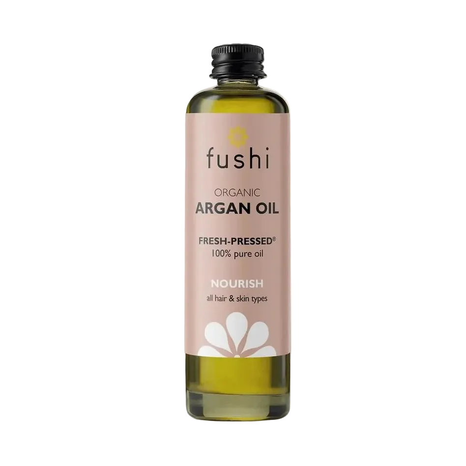 Bottle of Fushi organic argan oil on a light background. Label is soft pink with black text and white flower graphic, conveying a natural, nourishing tone.