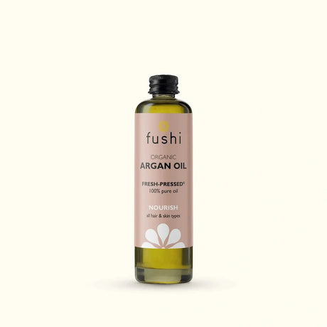 Bottle of Fushi organic argan oil on a light background. Label is soft pink with black text and white flower graphic, conveying a natural, nourishing tone.