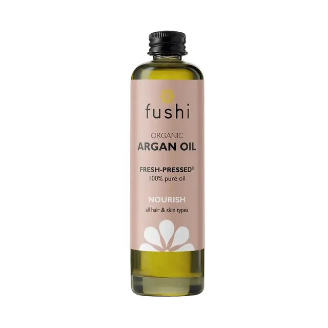 Bottle of Fushi organic argan oil on a light background. Label is soft pink with black text and white flower graphic, conveying a natural, nourishing tone.