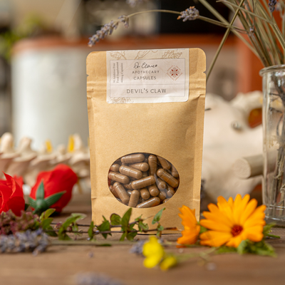 Package of 'Devil's Claw' capsules with a natural background featuring flowers and plants.