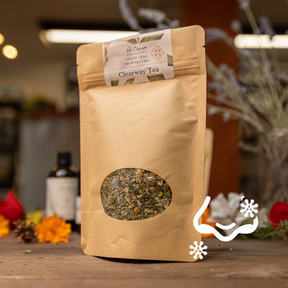 Tea package with a clear window showing tea leaves on a wooden surface with decorative elements.