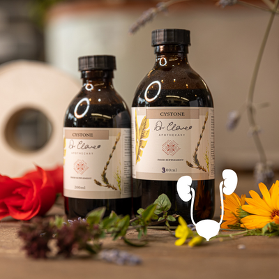 Two bottles of Cystone on a wooden surface with flowers and herbs.
