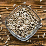 Overhead view of raw, shelled sunflower seeds in a square glass bowl set on a rustic wooden table.