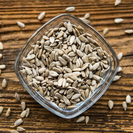 Overhead view of raw, shelled sunflower seeds in a square glass bowl set on a rustic wooden table.